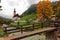 Beautiful autumn maple trees by the stream and a wooden bridge in front of a church with foggy mountains in the distant background