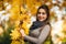 Beautiful autumn woman with autumn leaves on fall nature background. Branch with yellow leaves