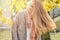 Beautiful autumn woman holding yellow maple leaf outdoors. Romantic girl with long hair in fall park