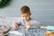 A beautiful baby boy sits on the kitchen table and helps his mother bake and decorate cookies