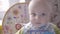 Beautiful baby boy at the table take a cookie in his hand, eating it, watching into the camera and babbling close up