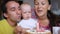 Beautiful baby celebrates first birthday. Young mother and father to help blow out the candle on the cake