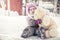 Beautiful baby embracing toy plush bear sitting on snow in park in cold sunny winter day during winter holidays