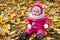 Beautiful baby girl one years old in pink jumpsuit sitting on yellow leaves - autumn scene. Toddler have fun outdoor in autumn