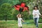 Beautiful background. Positive female child and grandmother running with red and black colored kite in hands outdoors