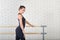 Beautiful ballerina weared in black bodysuit shoes posing at ballet class near barre, three quarter length portrait.