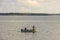 Beautiful Baltic sea landscape view. Men fishing from motorboat. Water surface merging with coast line and pale blue sky.