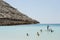 Beautiful beach resort with straw umbrellas on a blue sky and white clouds. On the background some people having fun on the beach