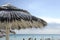 Beautiful beach resort with white straw umbrellas on a blue sky and white clouds. On the background some people having fun on the