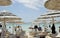 Beautiful beach resort with white straw umbrellas on a blue sky and white clouds. On the background some people having fun on the