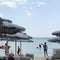 Beautiful beach resort with white straw umbrellas on a blue sky and white clouds. On the background some people having fun on the