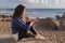 Beautiful black hair woman sitting on wooden embankment and using smartphone