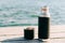 A beautiful black thermos of hot, herbal tea made from eco- friendly stainless steel stands on a wooden pier near the lake on a