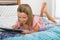 Beautiful blond 6 or 7 years old young girl lying on bed smiling happy using the internet on digital tablet pad watching and havin