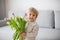 Beautiful blond boy, giving mother flowers and box with little gift for mothers day