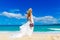 beautiful blond fiancee in white wedding dress with big long white train and with wedding bouquet stand on shore sea