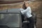 Beautiful blond lady in black striped high waisted pants and white blouse leaning on the top of her old car