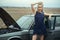 Beautiful blond lady in luxurious dark blue sequin tassel evening dress standing at her old car with open hood