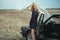 Beautiful blond lady in luxurious dark blue sequin tassel evening dress standing at her old car with open hood