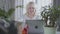 Beautiful blond mature woman sitting with laptop at home behind her gardening. Portrait of Caucasian retiree sitting