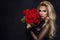 beautiful blond model in elegant dress holding a bouquet of red roses. Valentines`s gift on a black background