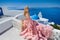 Beautiful blond runaway bride in white wedding dress fabulous with a very long train of crystals in the street on Santorini