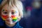 Beautiful blond toddler boy with rainbow painted on his face and messy hands