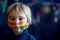 Beautiful blond toddler boy with rainbow painted on his face and messy hands