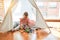 Beautiful blond toddler girl playing with constuction blocks inside tipi at kindergarten