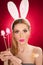 Beautiful blond woman as Easter bunny with rabbit ears on red background, studio shot. Young lady holding three colored eggs
