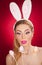 Beautiful blond woman as Easter bunny with rabbit ears on red background, studio shot. Young lady holding three colored eggs