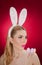 Beautiful blond woman as Easter bunny with rabbit ears on red background, studio shot. Young lady holding three colored eggs