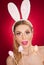 Beautiful blond woman as Easter bunny with rabbit ears on red background, studio shot. Young lady holding three colored eggs