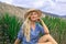 Beautiful blond woman in a hat. Sits outdoors on the prairie. Mysteriously smiling.