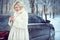 Beautiful blond woman in luxurious white fur coat drinking hot coffee on snowy winter day