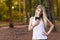 Beautiful blond young woman in park at sunset holding mobile near chest - Image