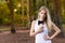 Beautiful blond young woman in park at sunset holding mobile near chest - Image