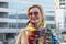 A beautiful blonde 40-45 years old in a coat and with a scarf on the background of urban multi-storey buildings.