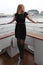 Beautiful blonde in a black dress and boots on a ship in the city. Wind on the river