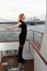 Beautiful blonde in a black dress and boots on a ship in the city. Wind on the river