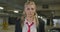beautiful blonde in a black suit, white shirt and red tie gets out of her black car in an underground parking lot