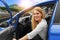 Beautiful blonde girl driving a car on the highway. Invitation to travel. Car rental or vacation.
