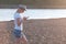 Beautiful blonde girl in a hat types a message on her mobile phone on the beach at sunset.