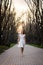 Beautiful blonde girl with long wavy curls in a white dress walk in evening the park among big trees.
