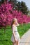 Beautiful blonde girl with long wavy curls in a white dress walk in the park among the pink trees, stunning makeup