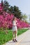 Beautiful blonde girl with long wavy curls in a white dress walk in the park among the pink trees, stunning makeup
