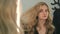 Beautiful blonde girl looks at herself in the mirror and straightens her long hair. Woman corrects her hair before a