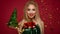 Beautiful blonde girl in a New Year`s image with Christmas bells around her neck and green tree. Beauty face with