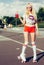 Beautiful blonde girl posing on a vintage roller skates in pink shorts and white T-shirt with a drink in a glass on a warm su