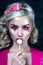 Beautiful blonde girl with two pigtails, with creative doll make-up: pink glossy lips, wearing pink skeleton dress licking lollipo